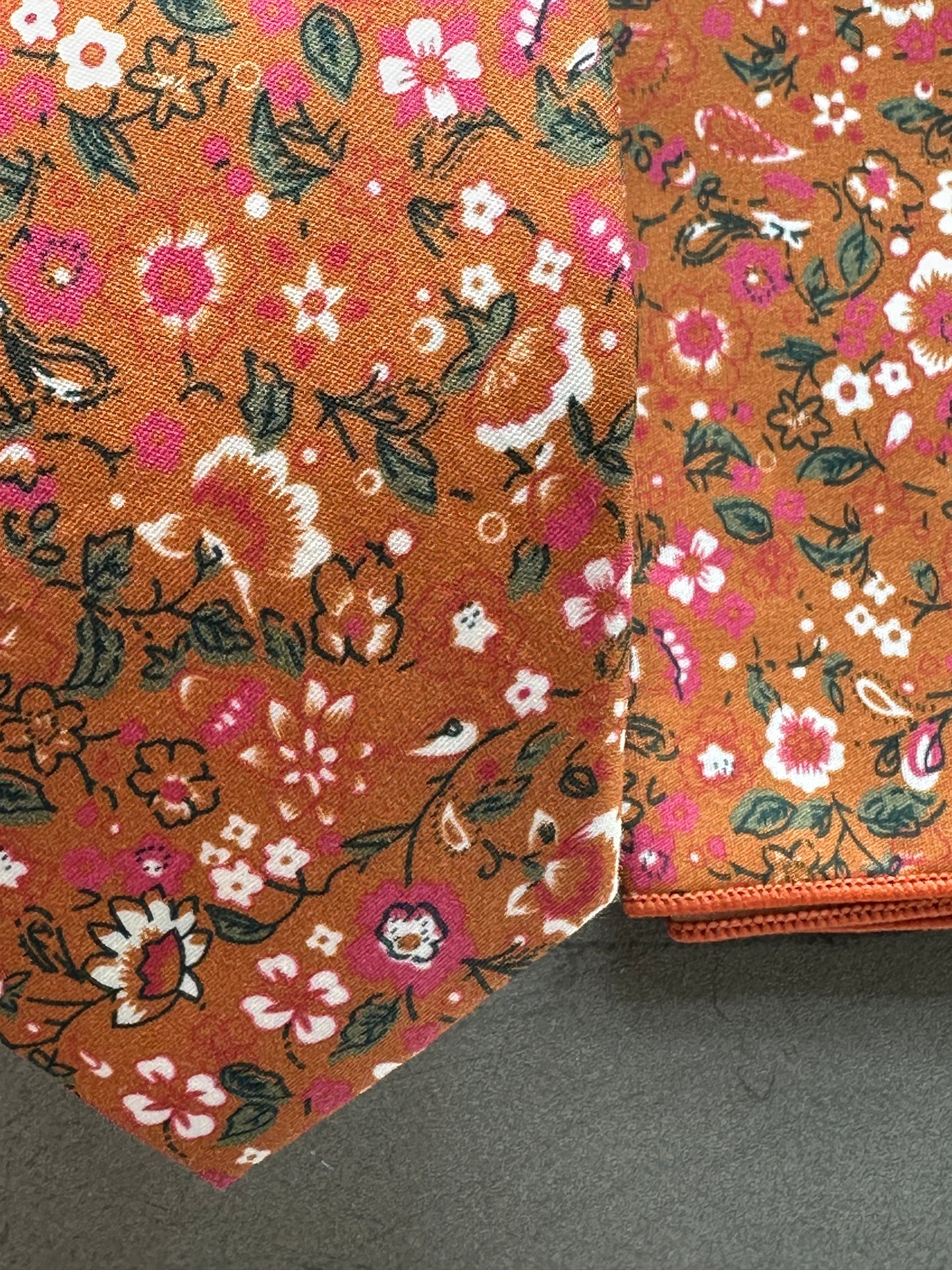 An image of a burnt orange floral tie with pink flowers and hints of green foliage.