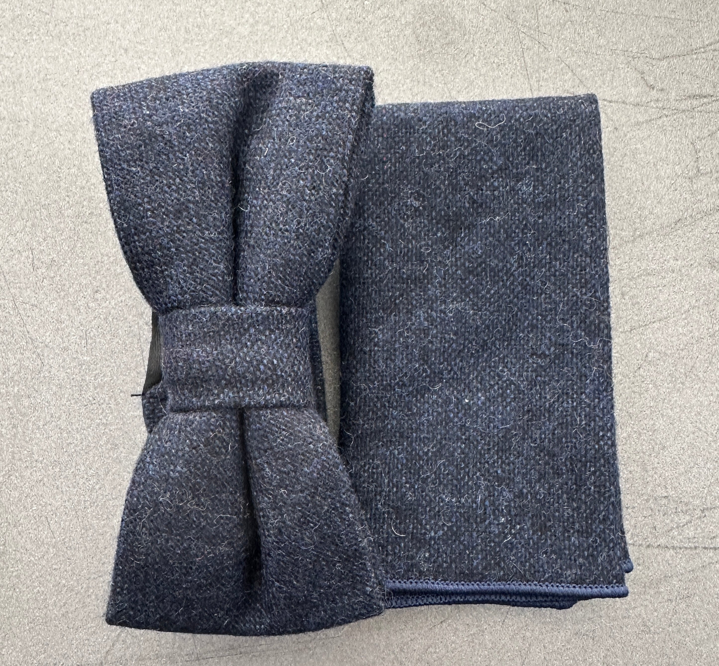 A close up photo of a navy blue mens bow tie and a blue pocket square ideal for many occasions including weddings.
