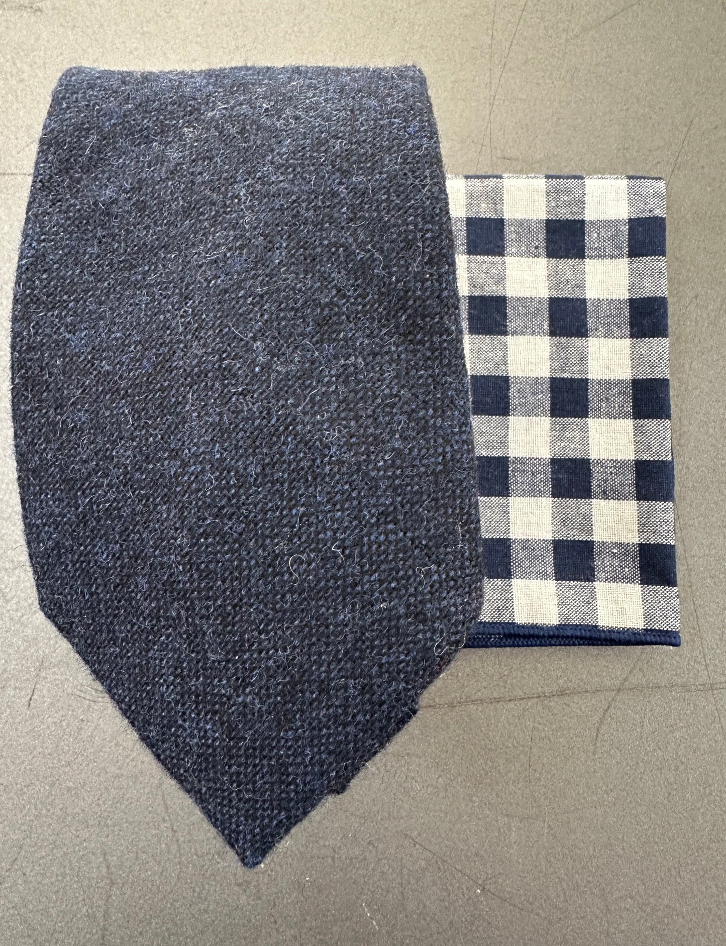 A photo of a navy blue mens tie and a blue checked pocket square ideal for many occasions including weddings. The pocket square makes an ideal edc hank.