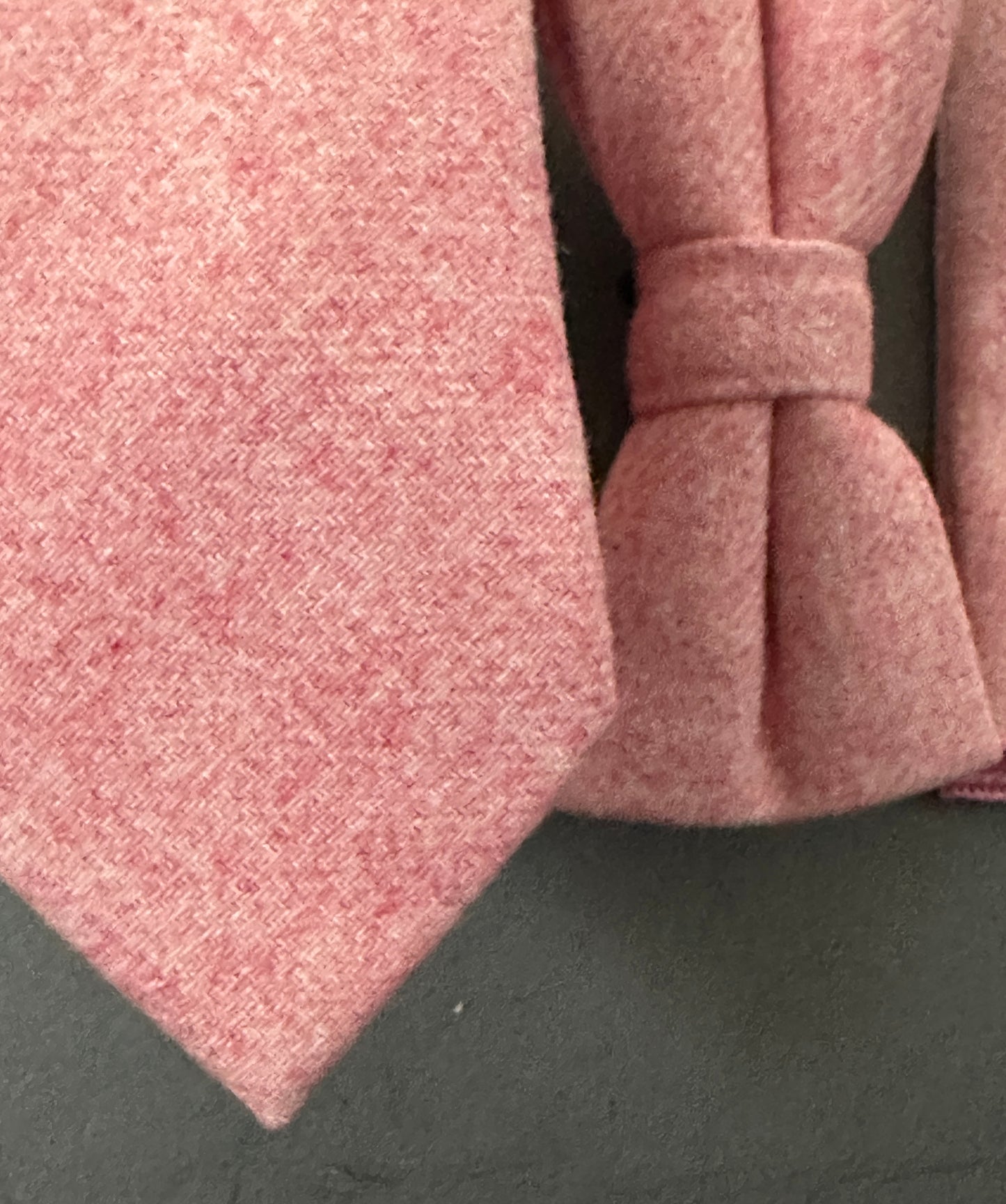 A close up photo of a pink tie bow tie and pocket square set in blush pink wool for grooms and groomsmen.