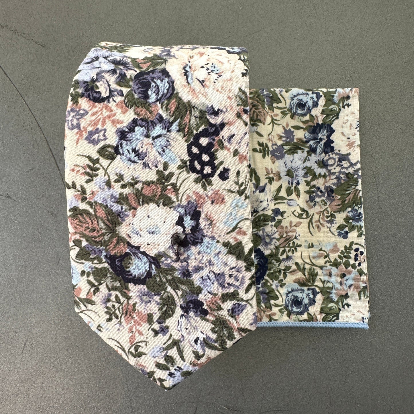 A Blue floral wedding tie and pocket square set for men in a blue floral print on a cream back ground.