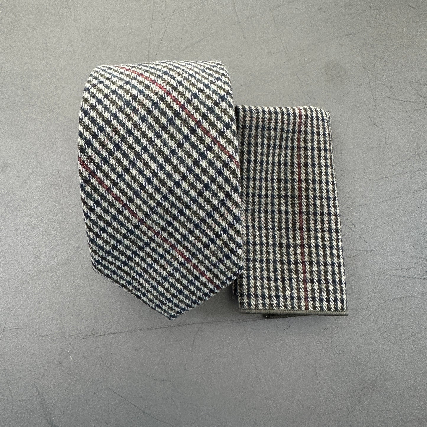 A grey wool checked tie and pocket square with hints of red and blue.