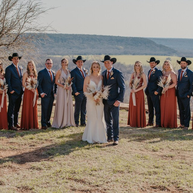 A group of grooms and groomsmen wearing burnt orange ties and pocket squares. The bridesmaids are wering burnt orange dresses.