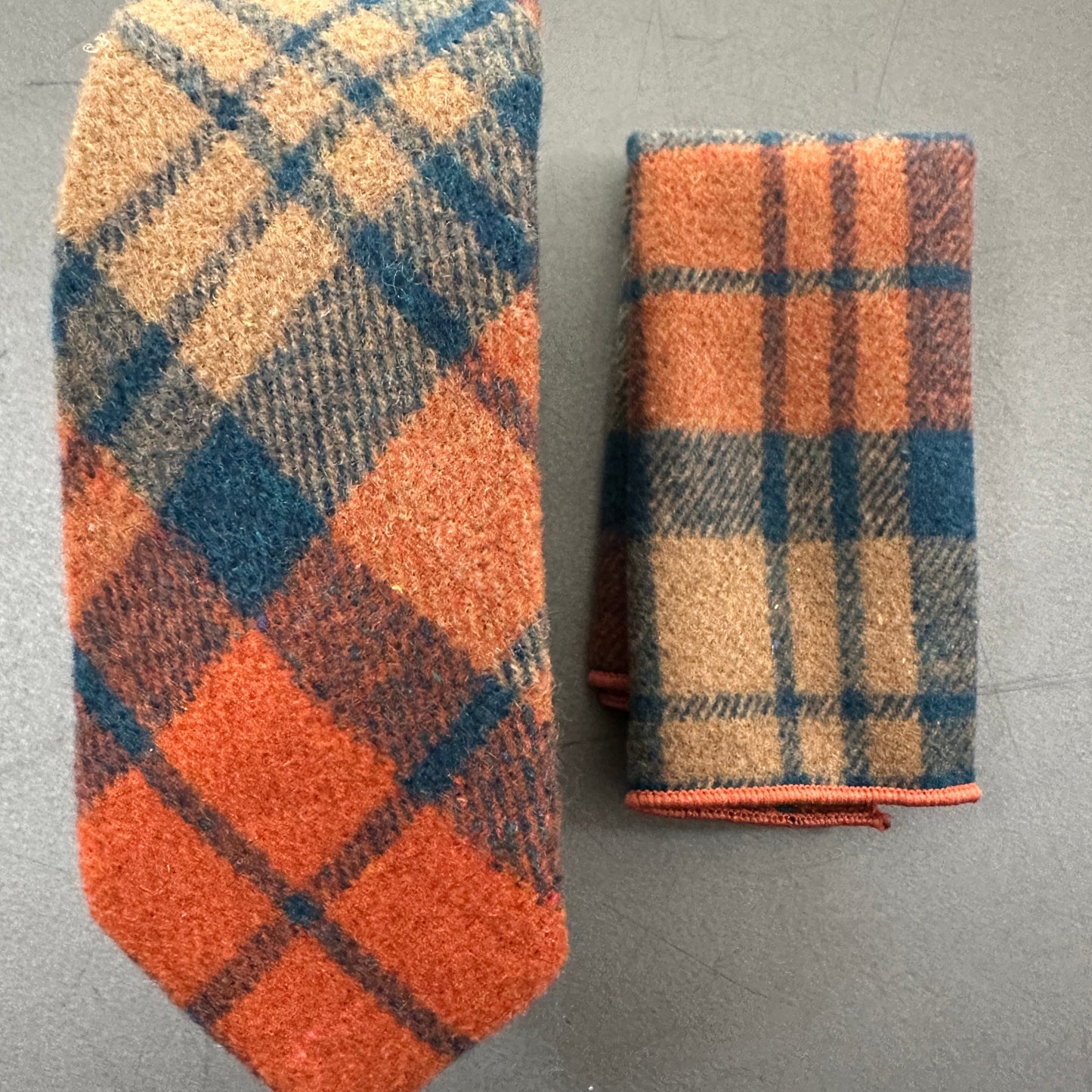 An orange wool tie with a navy check paired with a navy wool pocket square. The set makes an ideal gift for men or groomsmen and comes with free gift wrap.