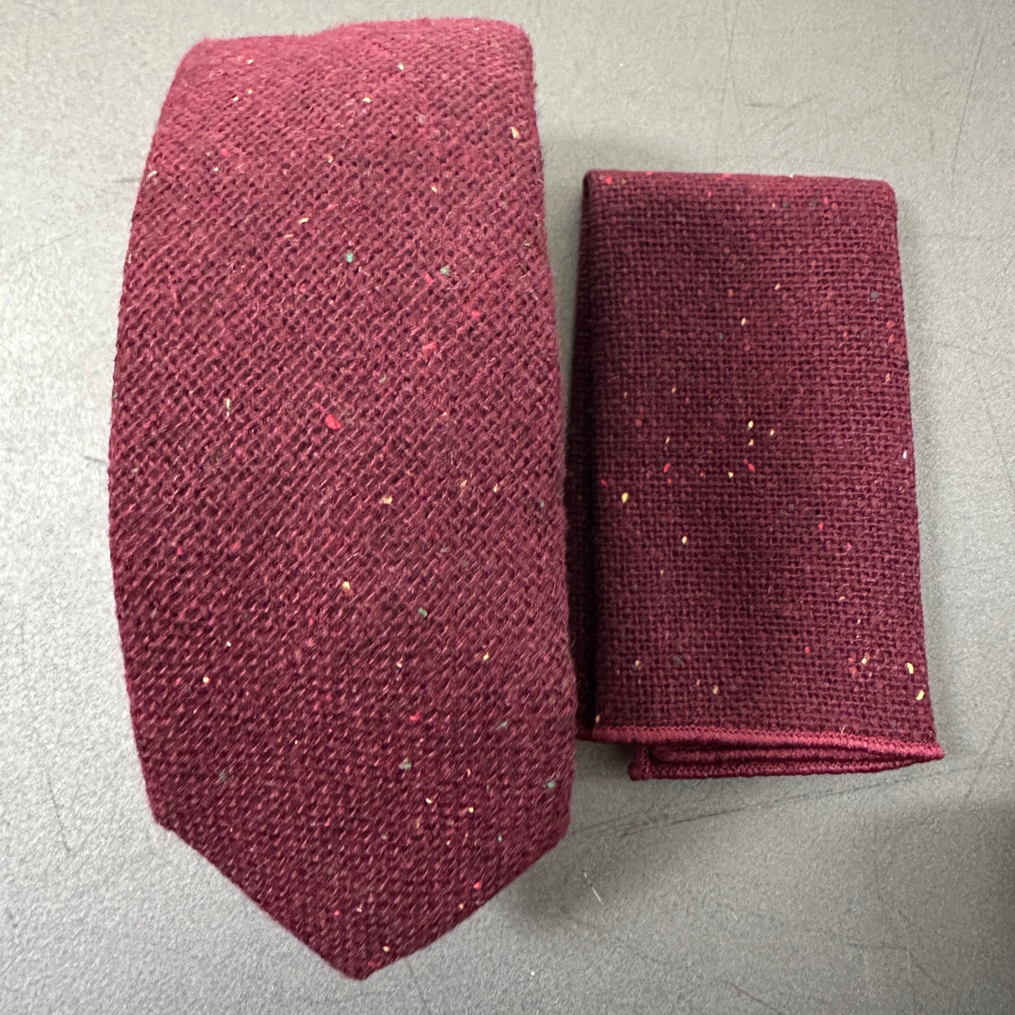 A deep red mens wool tie and pocket squares et with flecks in the fabric.