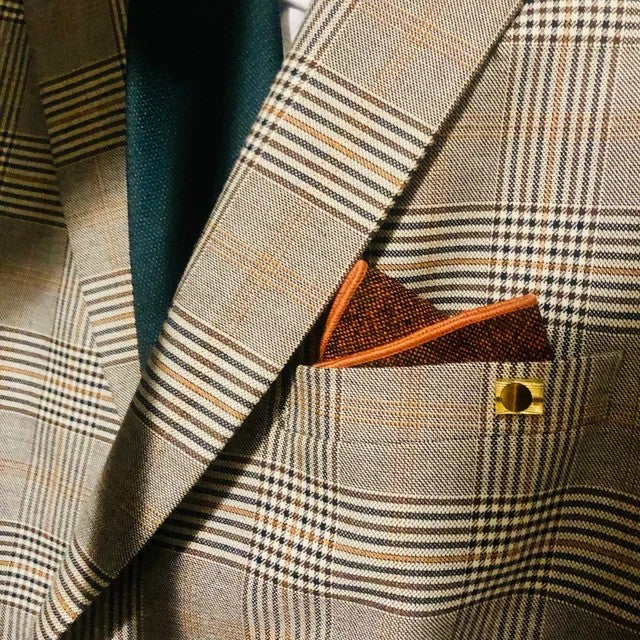 A photograph of a men's rust/ burnt orange handkerchief and pocket square worn with a green tie and checked suit. The pocket square has free gift wrapping and is perfect wedding attire or as a man's gift.