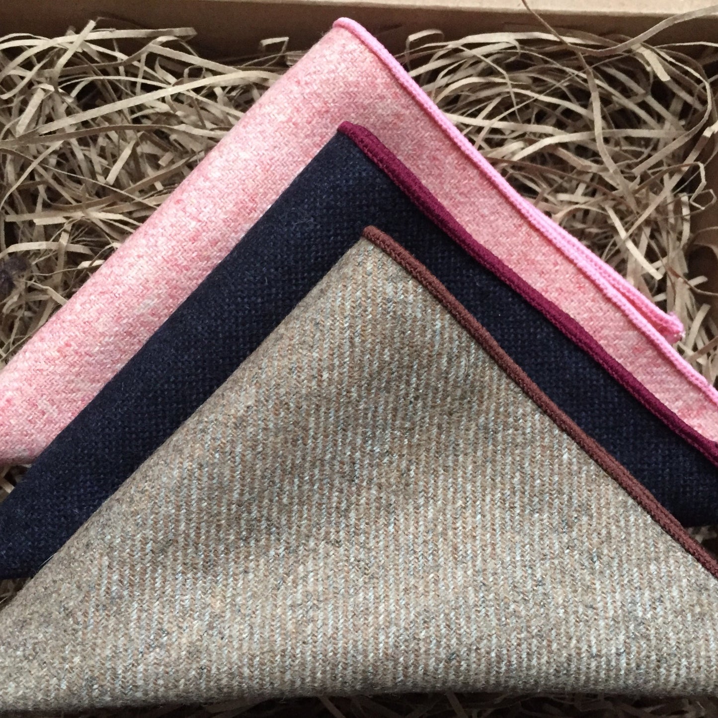 A photo of three inspired wool pocket squares in pink. navy blue and beige. The set makes a perfect gift for men as it is gift wrapped. t could also be a men's secret Santa gift, groomsmen or groom's gift. By Daisy and Oak Studio.