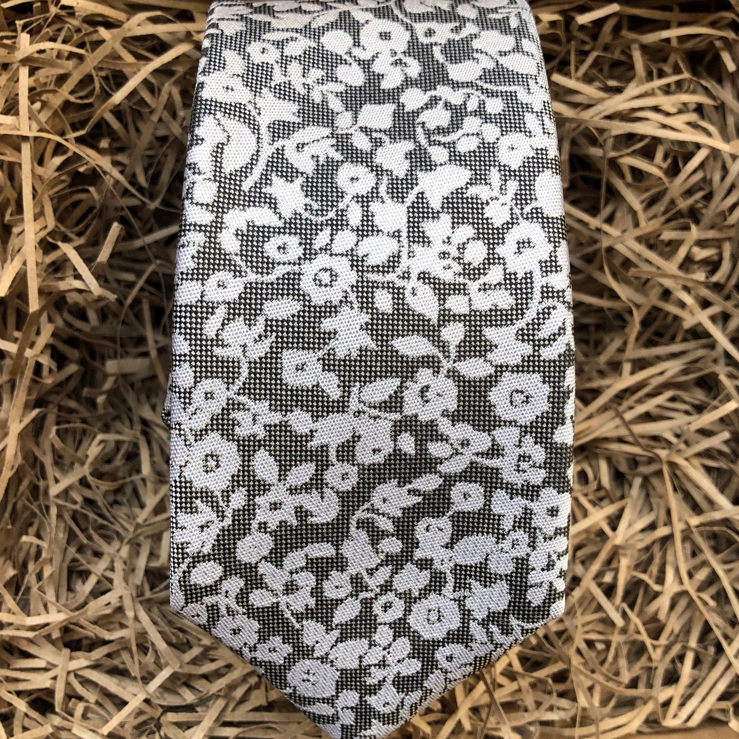 A silver grey tie with white flowers on a grey background. Ideal as a formal tie, wedding tie or for a special occasion. The tie is made by Daisy and Oak Studio and comes beautifully gift wrapped with free shipping.
