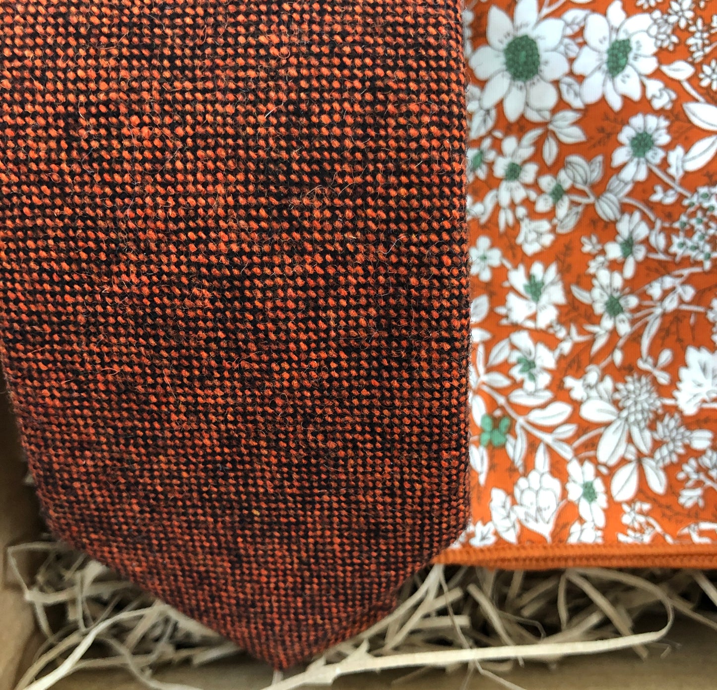 A photo of a burnt orange wool men's tie and pocket square. The tie is a flecked wool rust colour and the pocket square is in a floral orange cotton. The set comes with free gift wrapping and is handmade by Daisy and Oak Studio, UK
