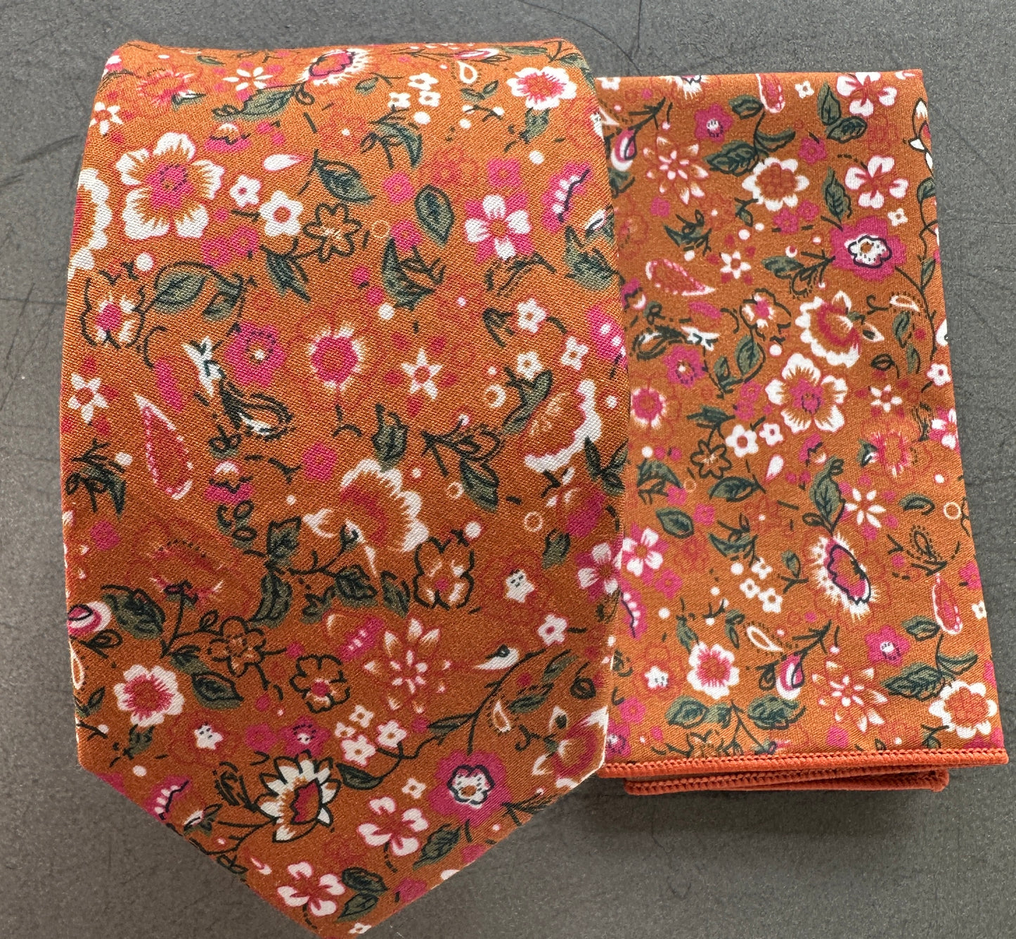 An image of an orange floral tie with pink flowers and hints of green foliage.