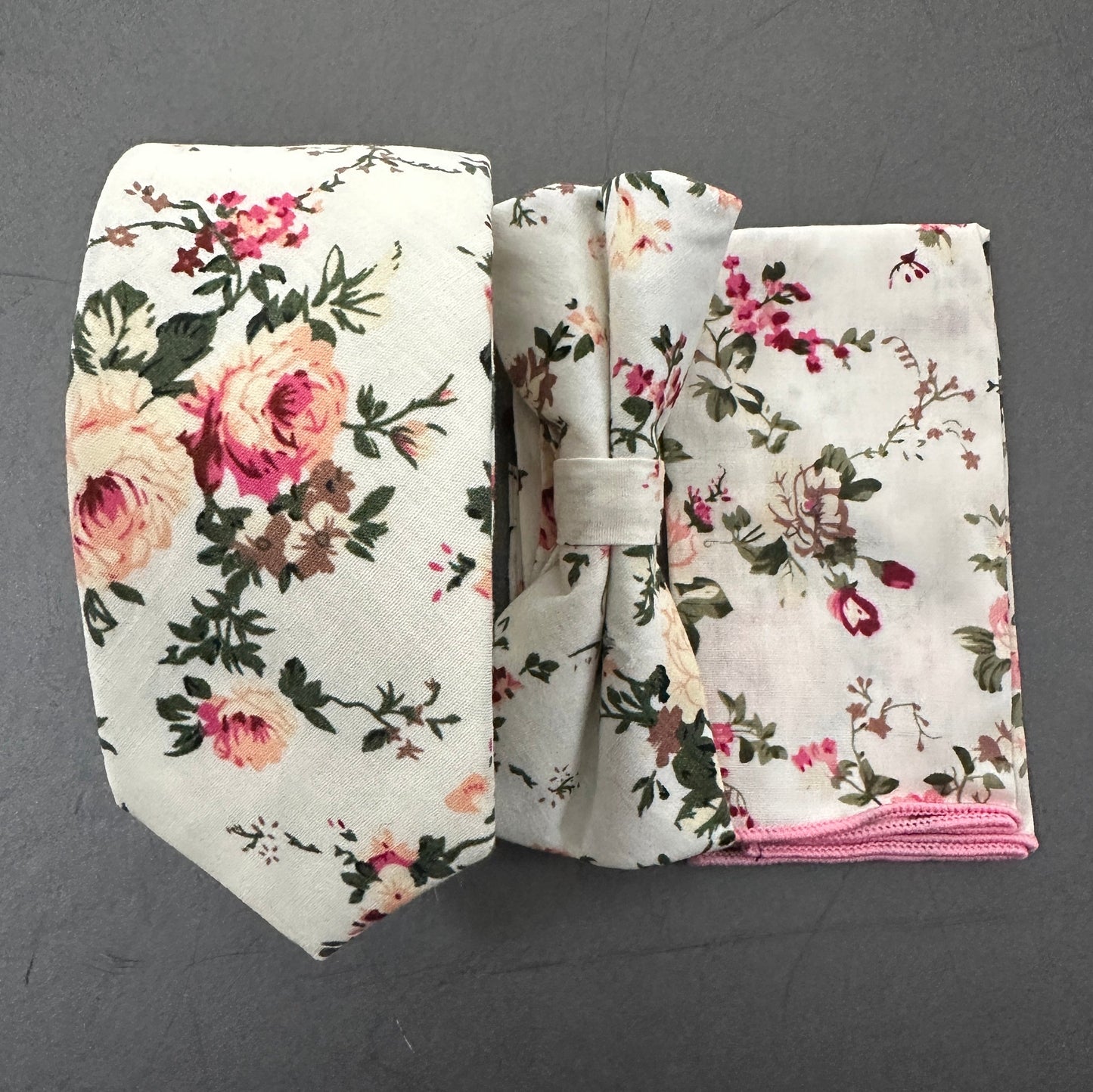 A pink rose. tie, bow tie and pocket square set for weddings. The set is made in cotton and is on a cream background.