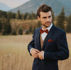 A man at a wedding wearing a burnt orange bow tie with matching rust pocket square. THis is the perfect wedding bow tie or men's gift wrapped Christmas present.