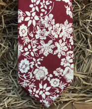Load image into Gallery viewer, A man&#39;s red floral necktie in cotton . This makes a handsome gift for christmas for men or for a groom and his groomsmen. The tie has a red background with white flowers.