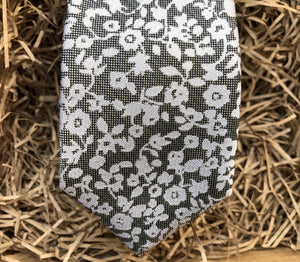 A close up of a silver grey tie with white flowers on a grey background. Ideal as a formal tie, wedding tie or for a special occasion. The tie is made by Daisy and Oak Studio and comes beautifully gift wrapped with free shipping.