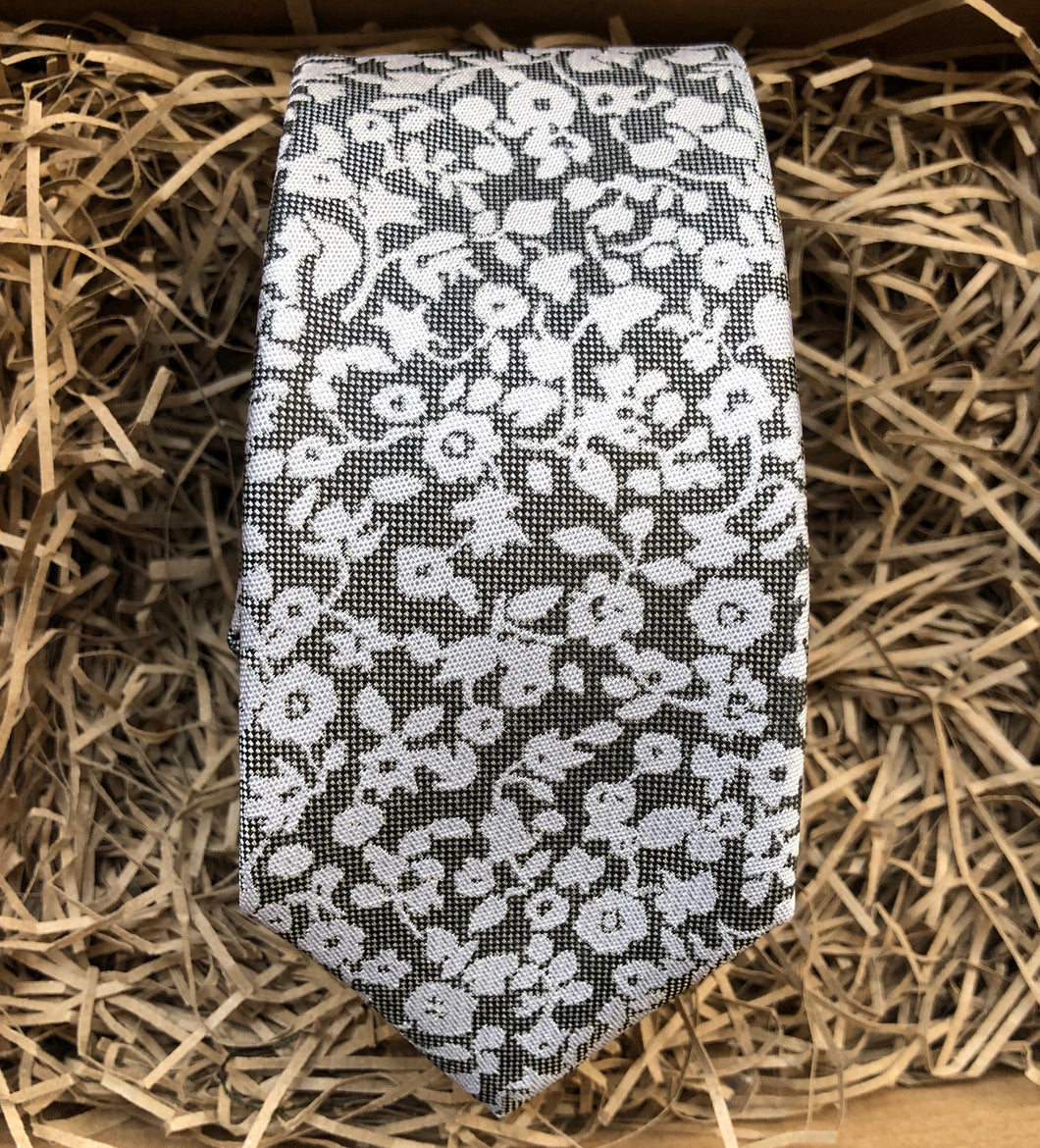 A silver grey tie with white flowers on a grey background. Ideal as a formal tie, wedding tie or for a special occasion. The tie is made by Daisy and Oak Studio and comes beautifully gift wrapped with free shipping.