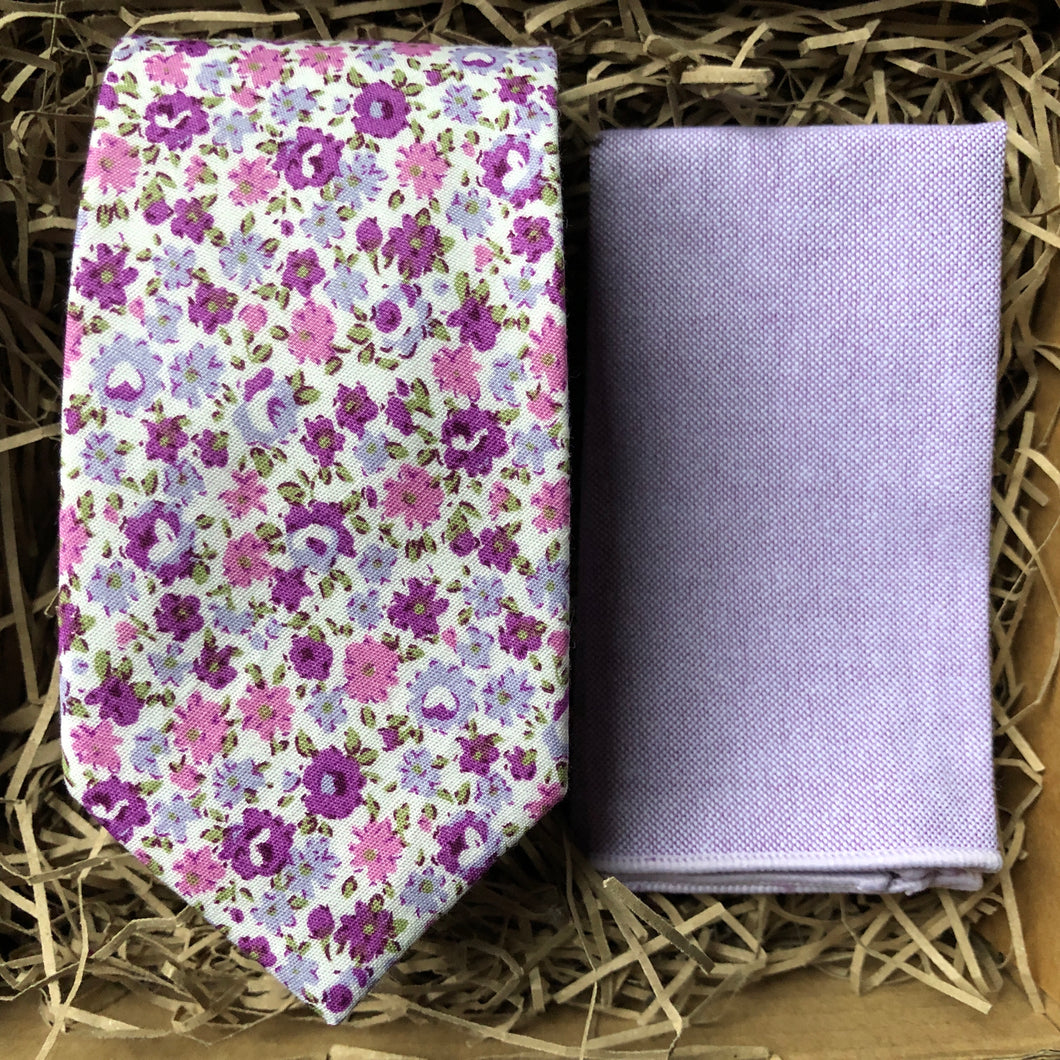 A lavender floral cotton men's tie with purple flowers and green accents matched with a navy suit. The ties are hand made by Daisy and Oak Studio and come gift wrapped so make ideal men's gifts and grooms and groomsmen ties.
