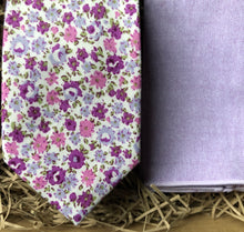Load image into Gallery viewer, A lavender floral cotton men&#39;s tie with purple flowers and green accents matched with a navy suit. The ties are hand made by Daisy and Oak Studio and come gift wrapped so make ideal men&#39;s gifts and grooms and groomsmen ties.