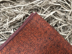 A men's burnt orange wool pocket square worn with a beige checked suit. THe pocket square comes gift wrapped and is handmade by Daisy and Oak Studio.