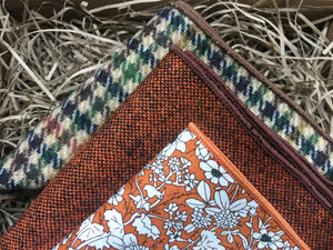A close up shot of a set of three pocket squares for men. The handkerchiefs are made of wool and in a burnt orange colour, a floral orange and a houndstooth check pattern in green and brow. THe pocket squares come with free gift wapping and make a fabulous men's Christmas gift, secret Santa gift or groomsmen's gifts. 