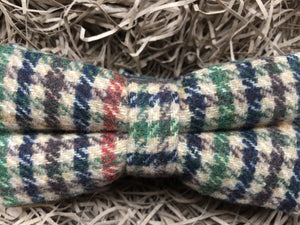 A close up shot of a houndstooth check men's bow tie in wool. THe checks are in a burnt orange, green, brown and navy colour. The bow tie comes gift wrapped and is perfect as men's gift or secret Santa. It is also often used as a groomsmen gift or grooms bow tie paired with a tweed suit.
