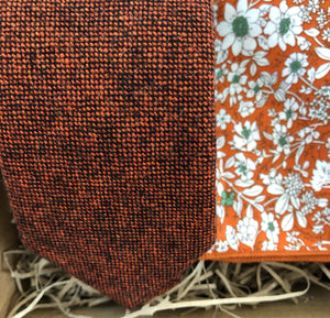 A photo of a  burnt orange wool men's tie and pocket square. The tie is a flecked wool rust colour and the pocket square is in a floral orange cotton. The set comes with free gift wrapping and is handmade by Daisy and Oak Studio, UK