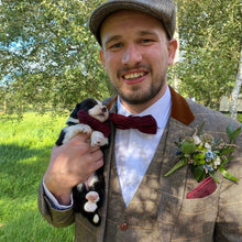 Load image into Gallery viewer, A groom wearing  the Oak bow tie which is a red flecked wool tie. The groom is holding a puppy who is also wearing the red tie. This has been handmade by Daisy and Oak and ships worldwide including to the USA